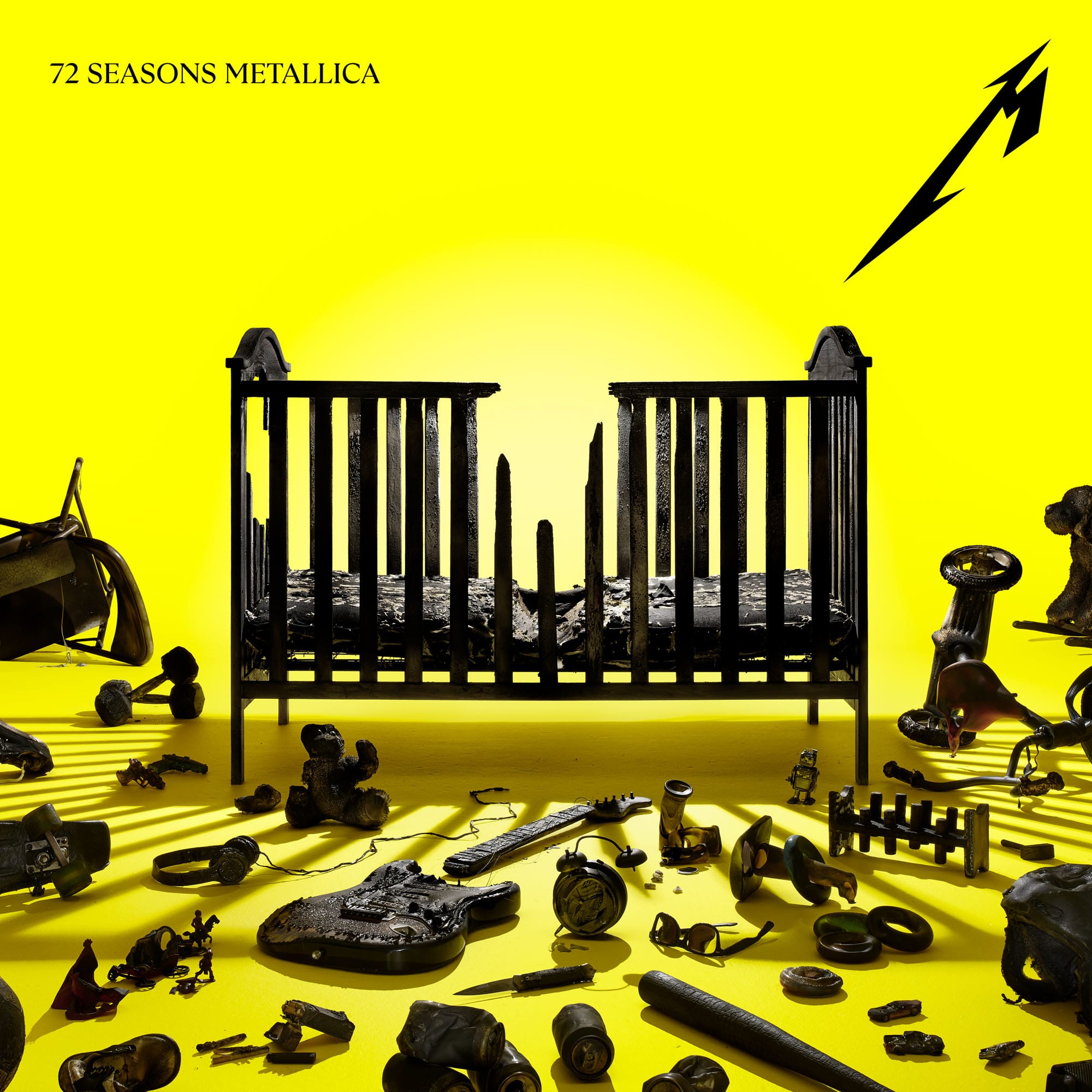 The cover art of Metallica's 72 Seasons. It features a prominent yellow background and foreground, with lots of burnt-black objects with a baby crib in the middle.